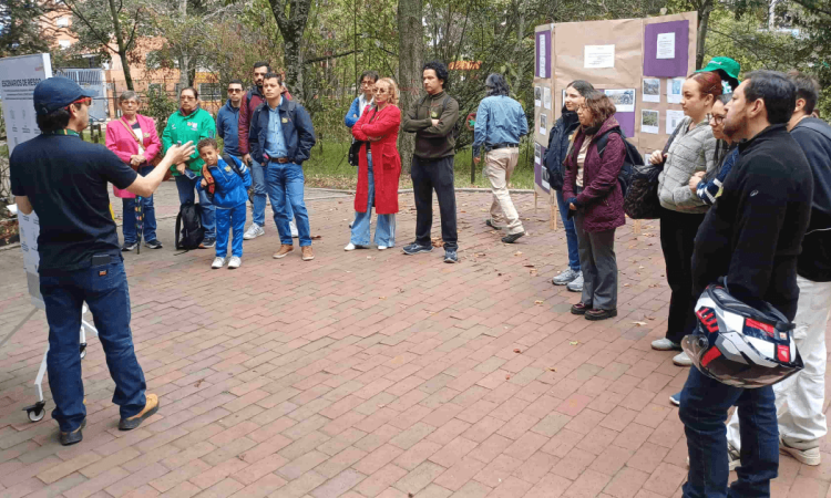 Personas participan en una actividad al aire libre sobre una plazoleta de ladrillo. Varias están alineadas y observan una demostración; algunas llevan chaquetas azules y una persona en el centro viste una chaqueta roja.