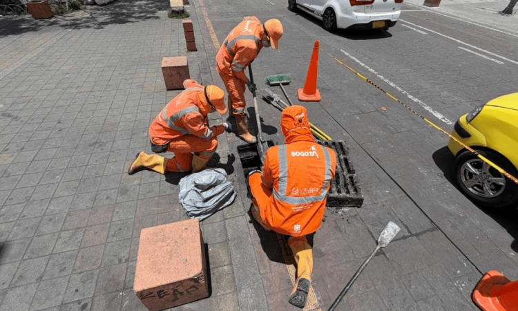 Foto que muestra tres personas con el uniforme de Aguas Bogotá limpiando un sumidero 
