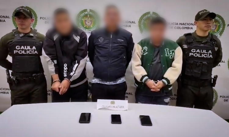 Foto de tres hombres capturados por la policía, escoltados por dos oficiales, uno en cada costado. 