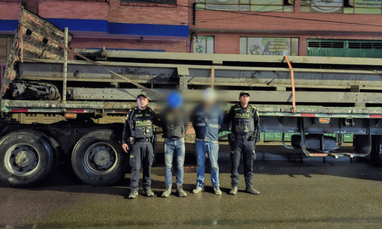Dos capturados en medio de dos Policías. Detrás está el camión con los 11 rieles incautados.