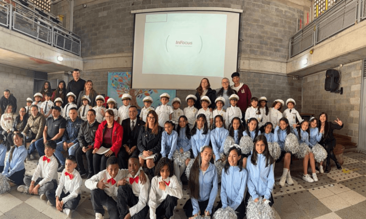Grupo de estudiantes y docentes de Teusaquillo posa para una fotografía grupal en un espacio interior de un colegio. Al fondo se observa una pantalla de proyección y un muro de ladrillo, mientras los participantes están ubicados en varias filas frente a la cámara