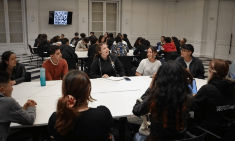 Foto que muestra estudiantes sentados en una mesa hablando 