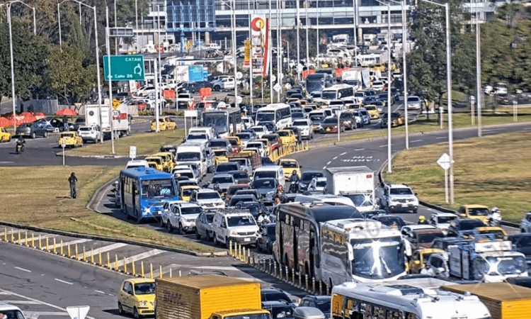 Alta congestión vehicular en avenida El Dorado de Bogotá con filas de carros, buses, camiones y motocicletas avanzando lentamente entre varios carriles. Se observan separadores viales, señalización y tránsito denso en ambos sentidos.