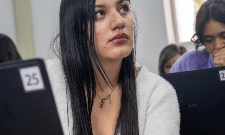 Foto de una mujer con otras dos de fondo, en un salón de clases.