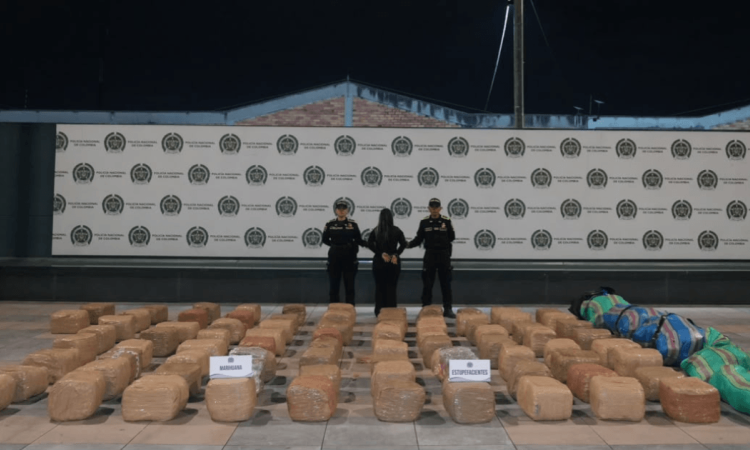 Foto de una persona capturada en medio de dos policías, con e cargamento de 700 kg de marihuana expuestos en el piso. 