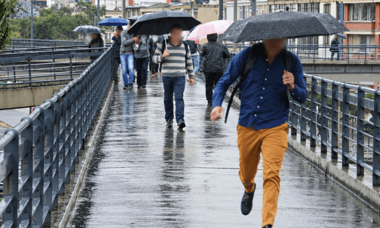 Personas caminan bajo la lluvia por una vía de Bogotá mientras una de ellas sostiene una sombrilla negra y otras transitan por un andén mojado durante fenómeno de El Niño 2026.