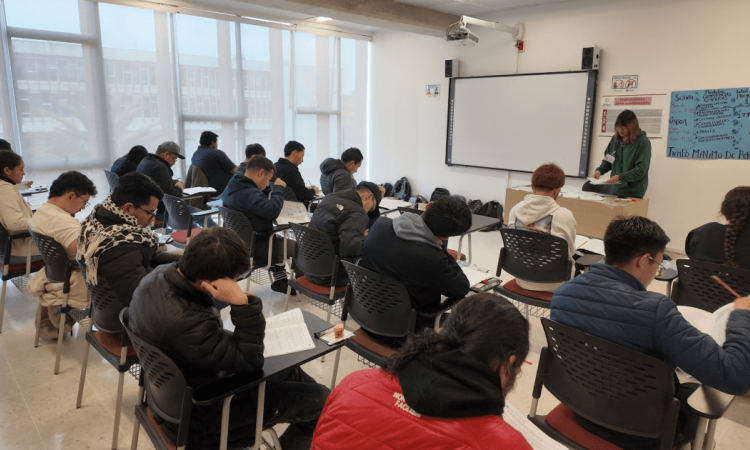 Foto que muestra personas sentadas en escritorios en un salón de clases