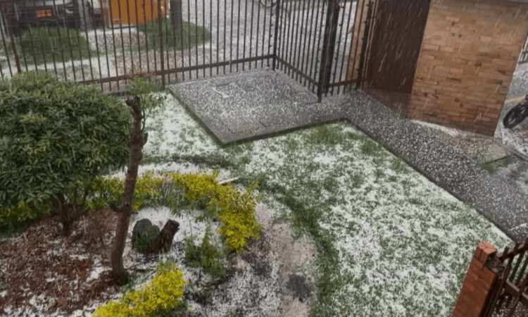 Granizada en Bogotá acumulada sobre el suelo de un patio con jardineras, mientras una estructura metálica y una cerca permanecen rodeadas por la capa blanca.