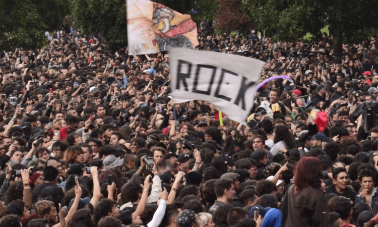 Multitud de asistentes reunidos al aire libre durante Rock al Parque en Bogotá. En el centro se observa una bandera blanca con la palabra “ROCK”, mientras cientos de personas ocupan gran parte del espacio frente al escenario, rodeadas por árboles.