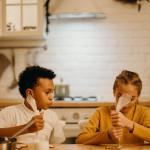 Una niña rubia y un niño moreno decoran postres en una cocina.