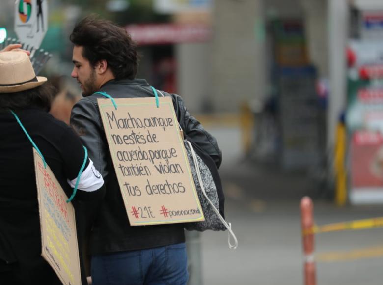 Joven con un cartel en su espalda que reza: "Marcho aunque no estés de acuerdo porque también violan tus derechos".