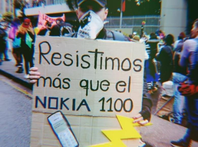 Joven con un cartel que reza: "Resistimos más que el Nokia 1100".