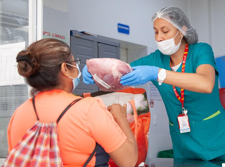 Funcionaria entregando ayuda de carne a una beneficiaria.