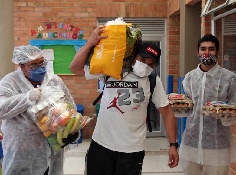 Ciudadano sale de las instalaciones donde se entregan los mercados, sacando el suyo en sus hombros.