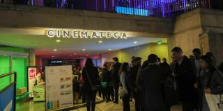 La fachada de la Cinemateca de Bogotá, de noche, con una fila de personas esperando para entrar
