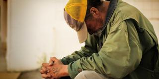 perfil de un hombre de avazada edad en situación de tristeza y pobreza sentado con cabeza abajo y manos cruzadas