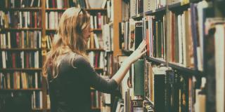 Una mujer recorre con la mano una estantería llena de libros 