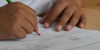 Las manos de un niño escribiendo con lápiz rojo en una hoja en blanco 