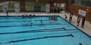 Plano general de una piscina, hay varios niños entrenando en la piscina con sus profesoras afuera guiándolos en Ciudad Bolívar