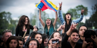 Un grupo de jóvenes rockeros disfrutan de Rock al Parque mientras sostienen una bandera de Colombia.