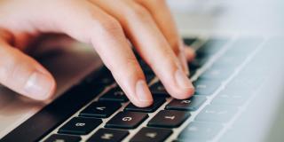Imagen Ilustrativa. Manos de una persona blanca sobre un teclado de computador gris con botones negros.