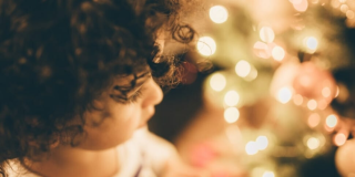 Imagen ilustrativa. Niño blanco de cabellos crespos mira un árbol de Navidad.