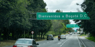 Foto de la entrada a Bogotá por una vía rodeada de árboles y un cartel que da la bienvenida