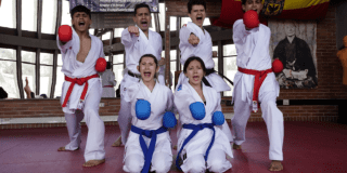 Imagen de cuatro hombres vestidos con traje de karate y dos mujeres de rodillas en salón de practica de boxeo