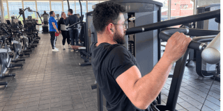 Imagen de hombre haciendo ejercicio en máquina, al fondo se ven más personas ejercitándose