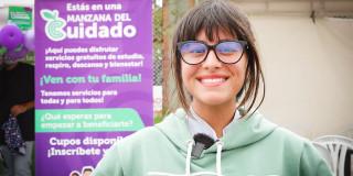 En la foto una mujer sonriendo y atrás un cartel con los servicios de la secretaría de la mujer