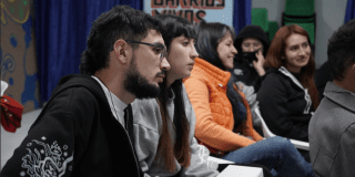 Imagen de varias personas, que sentadas prestan atención a alguien que esta de frente. 