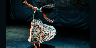 Imagen de una mujer danzando en un escenario cuyo fondo es de color gris oscuro.