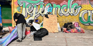 Foto de una persona que organiza pertenencias y materiales en medio de residuos acumulados junto a un muro