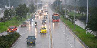 Imagen de una vÍa principal de Bogotá por la que circulan diferentes tipos de vehículos mientras llueve.