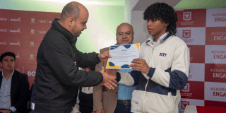 Imagen de un estudiante recibiendo un diploma simbólico de la beca