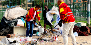 Foto de dos trabajadores de la Alcaldía Local de Kennedy, vestidos con chaquetas rojas, realizando labores de limpieza y recolección de basura en un espacio público
