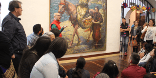 Imagen de varias personas en sala de un museo escuchando atentamente al guía.