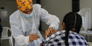 Imagen de enfermera que coloca vacuna a una mujer que está sentada.