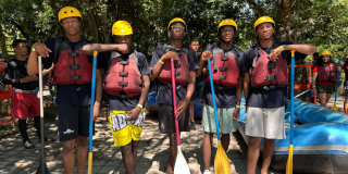 Foto de grupo de jóvenes con chalecos y cascos que se prepara para una actividad de rafting al aire libre.