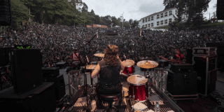 Imagen de una banda de rock en el escenario, de frente se encuentran muchas personas en el público