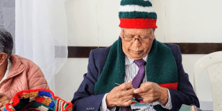 Imagen de una persona mayor tejiendo una bufanda navideña