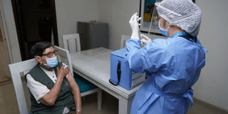 Imagen de una mujer sentada mientras una enfermera prepara una vacuna