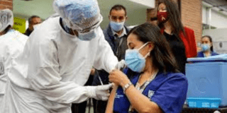 Imagen de una enfermera vacunando a una mujer sentada, las dos usan tapabocas