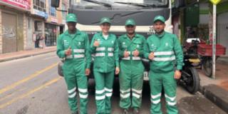 Foto de un grupo de operarios y operarias de aseo en Bogotá, al lado un camión recolector de basuras.