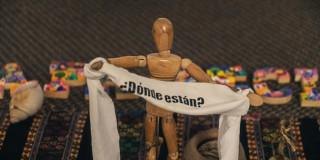 Figura de madera con una cinta en la que se lee "¿Dónde están?".