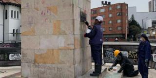 Foto que muestra un monumento de la ciudad y tres personas limpiandolo
