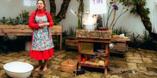 Imagen de una mujer campesina en un patio de una casa donde se ven artículos de mesa y cocina