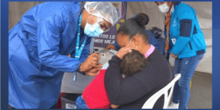 Imagen de una enfermara vacunando a un niño mintras su mamá lo carga en sus brazos.