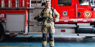 Mujer Bombera frente a un camión de bomberos.