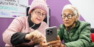 Dos mujeres mayores utilizando un celular en un proceso de capacitación en Bogotá.